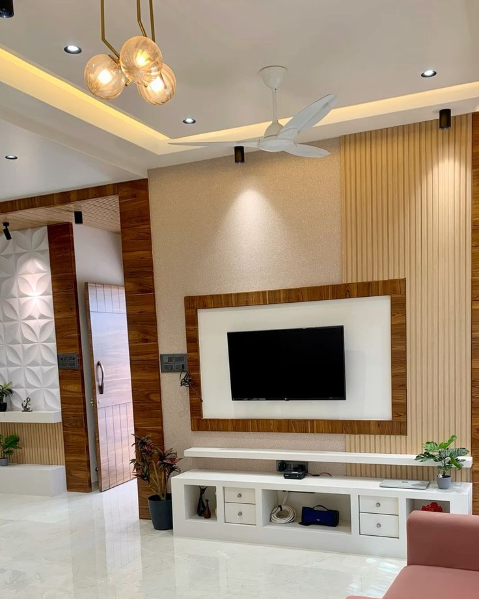 1 TV wall with a wood-look frame, cream fluted panels and a white storage console beneath warm ceiling lighting.