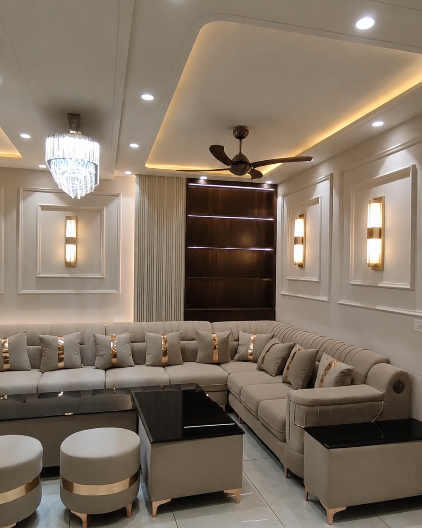 Beige sectional sofa with gold accented cushions, black-topped tables, decorative wall mouldings and a crystal style chandelier.