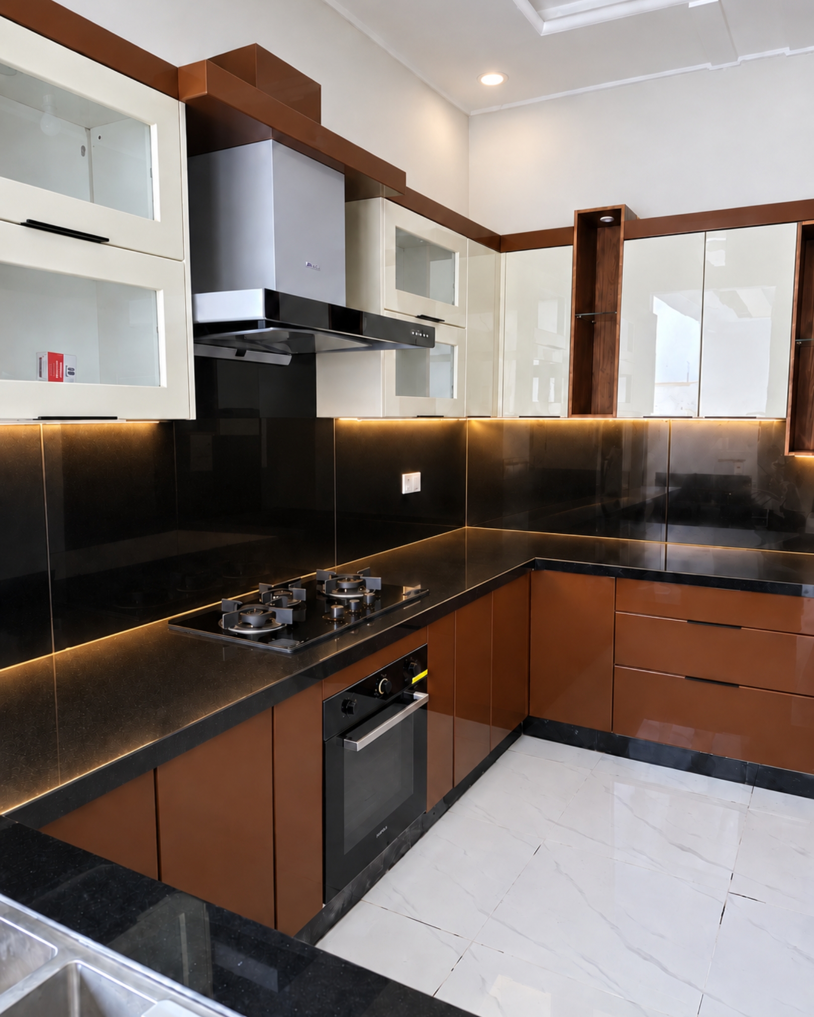 Angled kitchen view showing brown and cream cabinetry, black countertops, a chimney hood, built in oven and a wood look display niche.