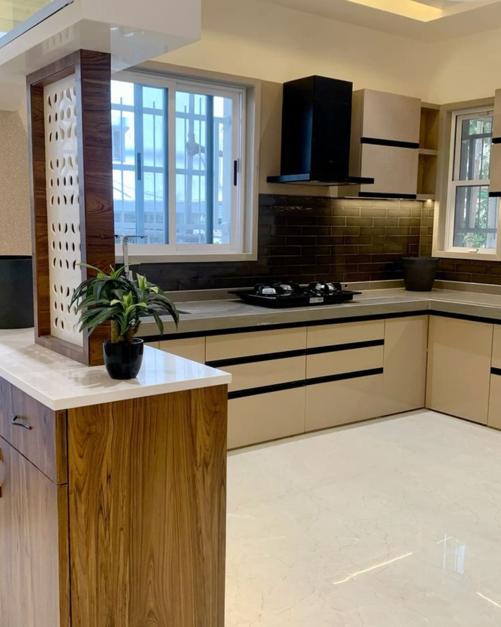 2 Cream kitchen cabinets with black trim, light countertops, a dark brick-pattern backsplash and a wood-look partition.