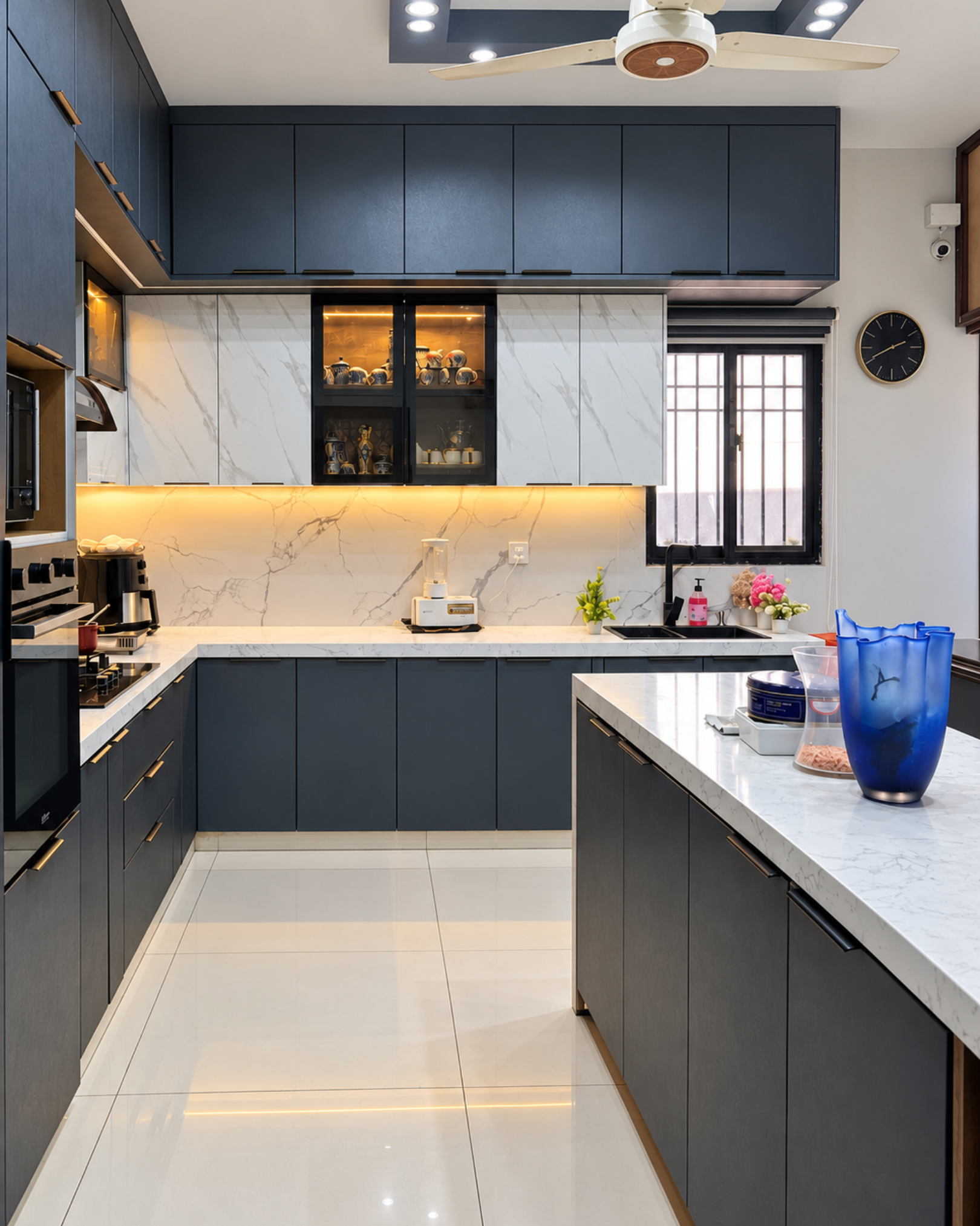 Charcoal kitchen with illuminated glass cabinets, marble effect backsplash and a black sink beneath the window.