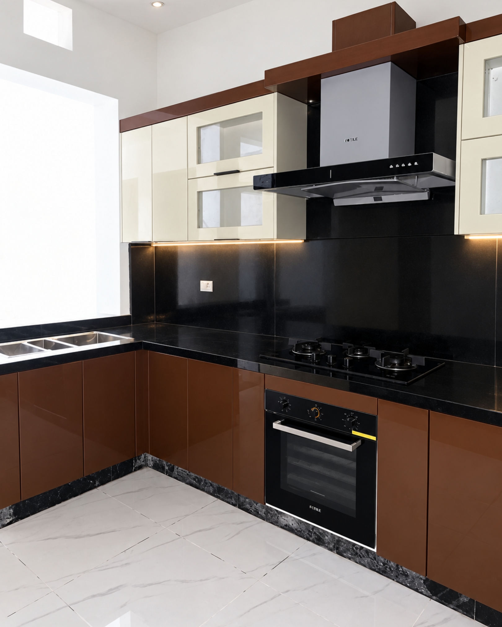 Brown and cream kitchen with a double sink beside a bright window opening, black countertops, a gas hob and warm under-cabinet lighting.