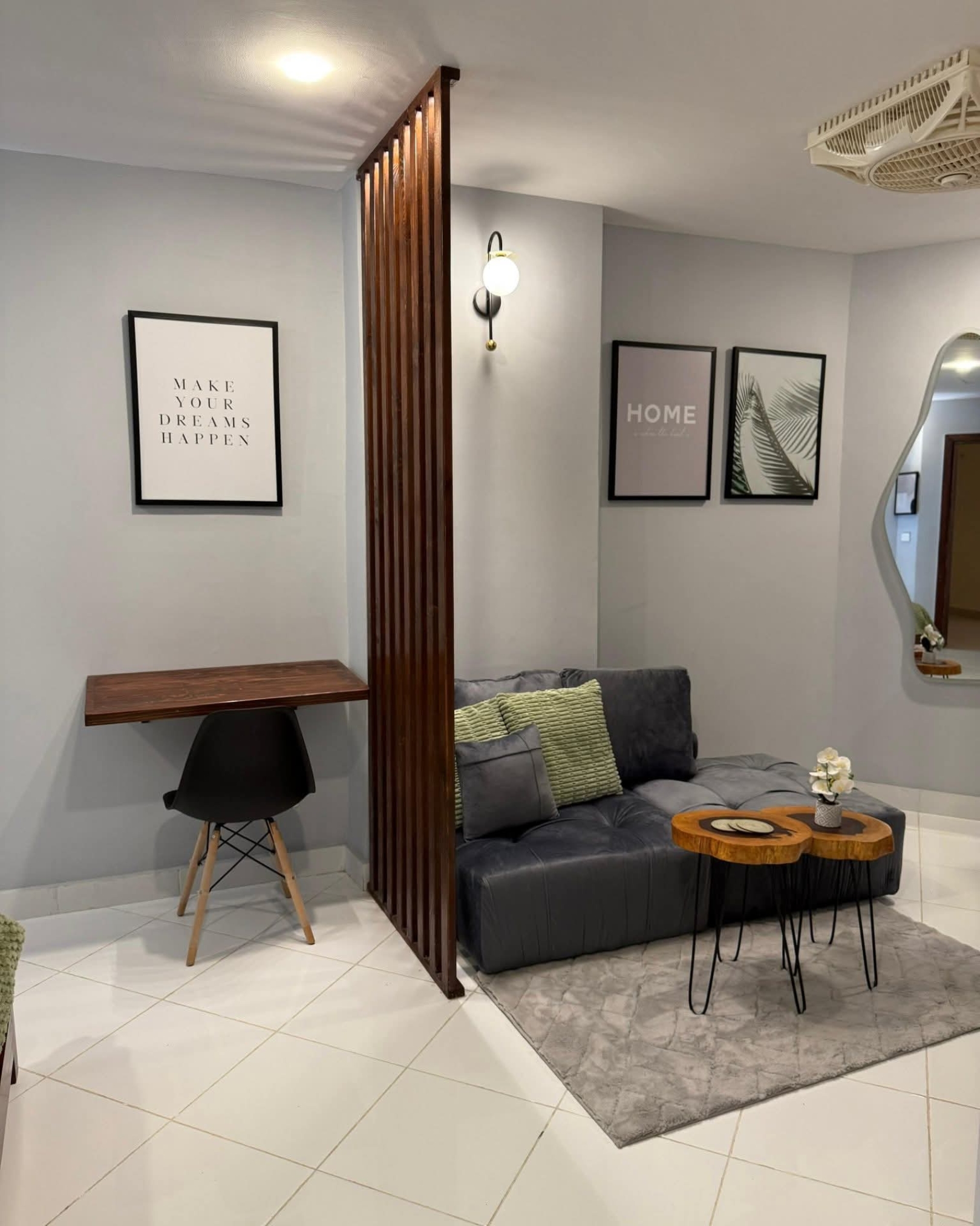 3 Wooden slat partition separating a floating study desk and black chair from a cozy grey seating area.