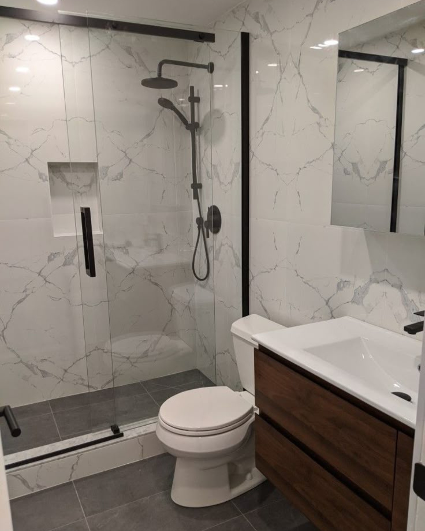 Bathroom with white marble-effect tiles, a wood-look vanity, black shower fittings and a glass shower enclosure.