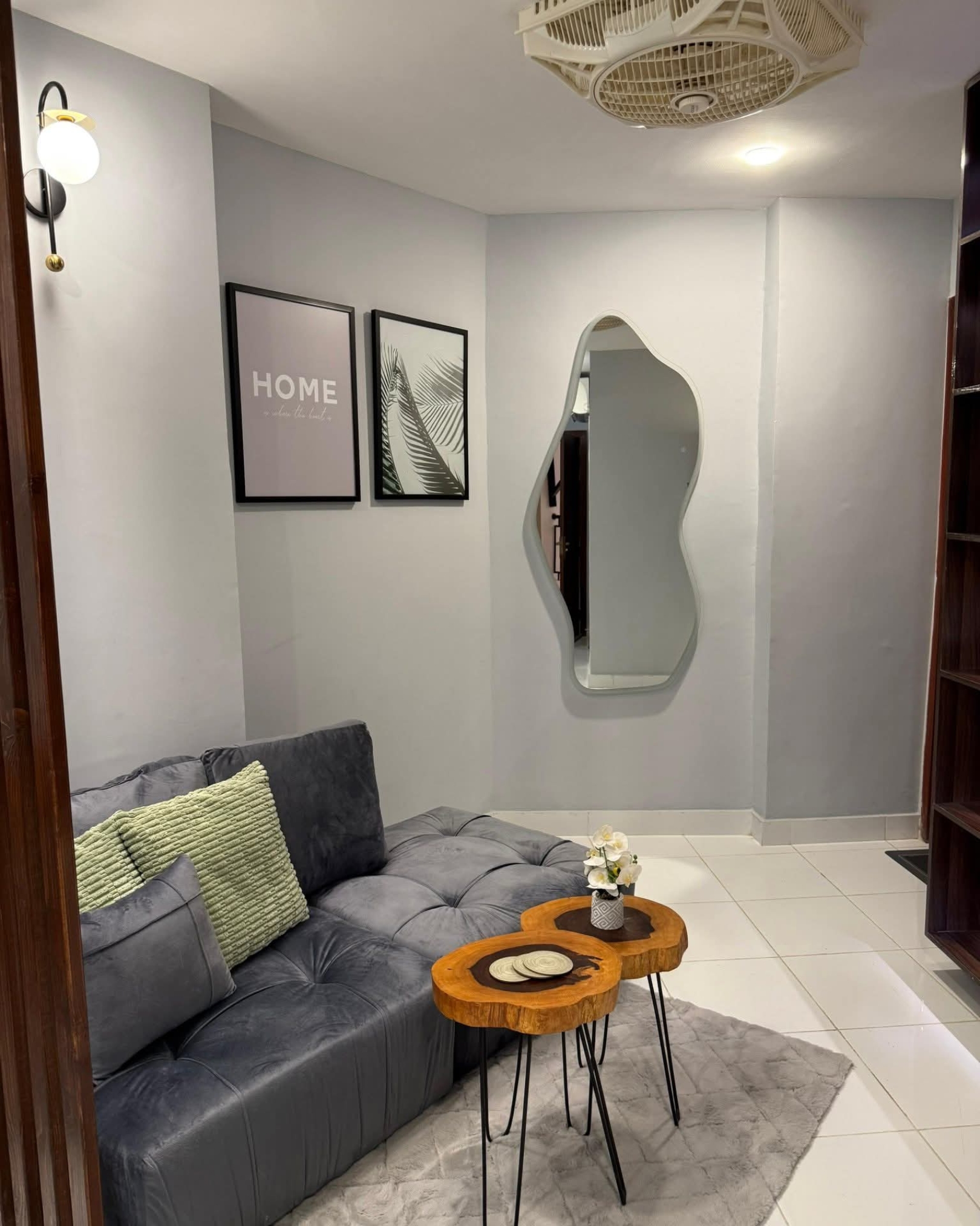 4 Grey chaise sofa and wooden coffee tables beneath framed prints, with an irregular mirror on the light grey wall.