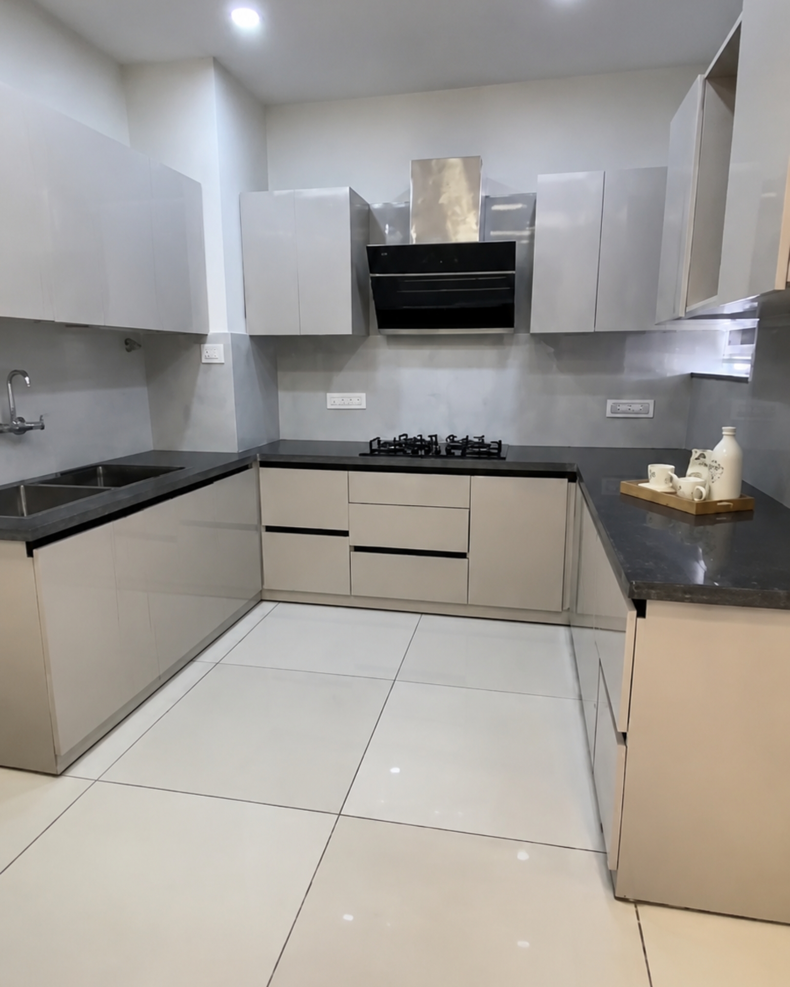 4 U-shaped kitchen with glossy light cabinets, dark countertops, grey backsplash, double sink and black extractor hood.