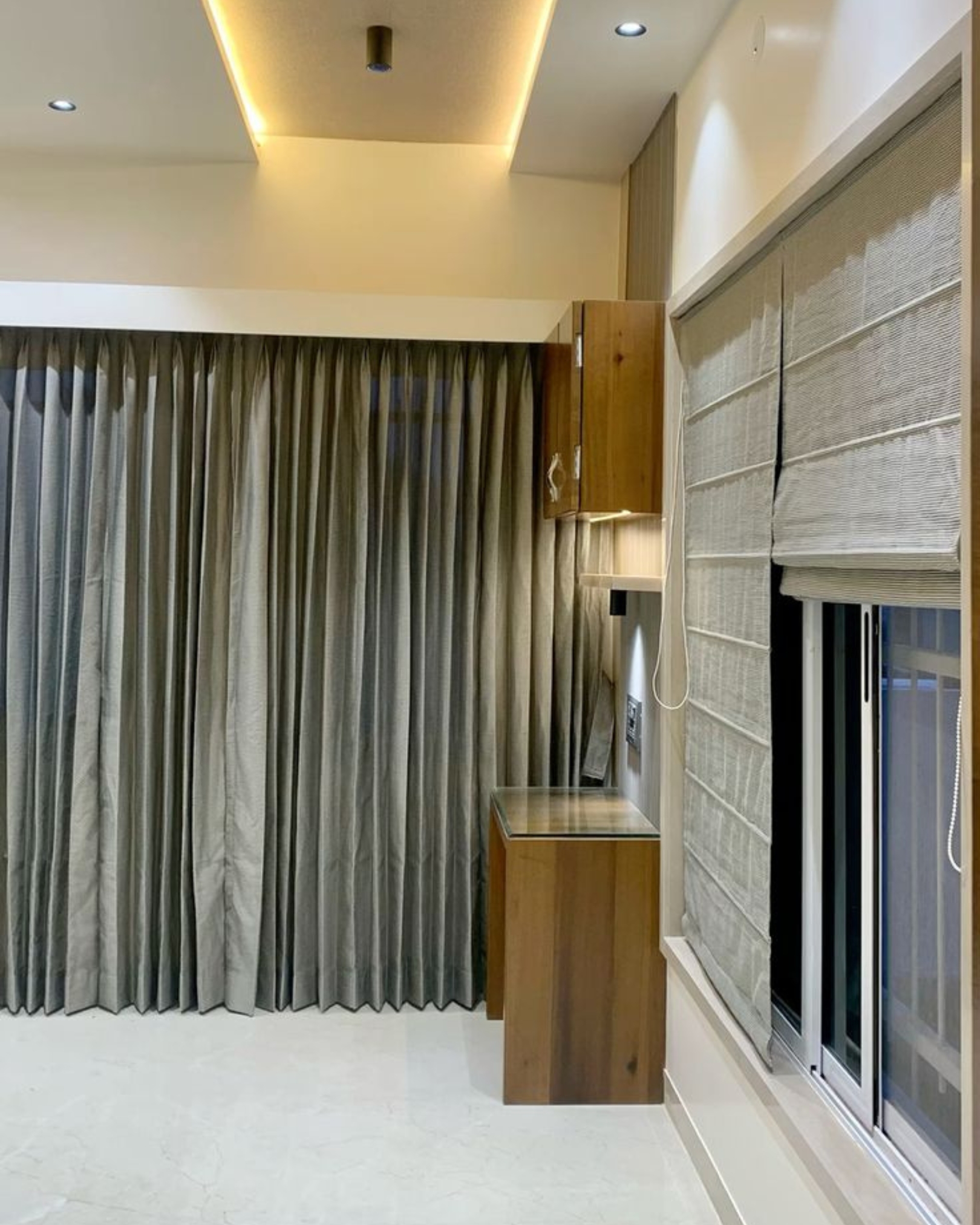 4 Compact wood-look dressing table with a mirror and overhead cabinet beside grey curtains and Roman blinds.