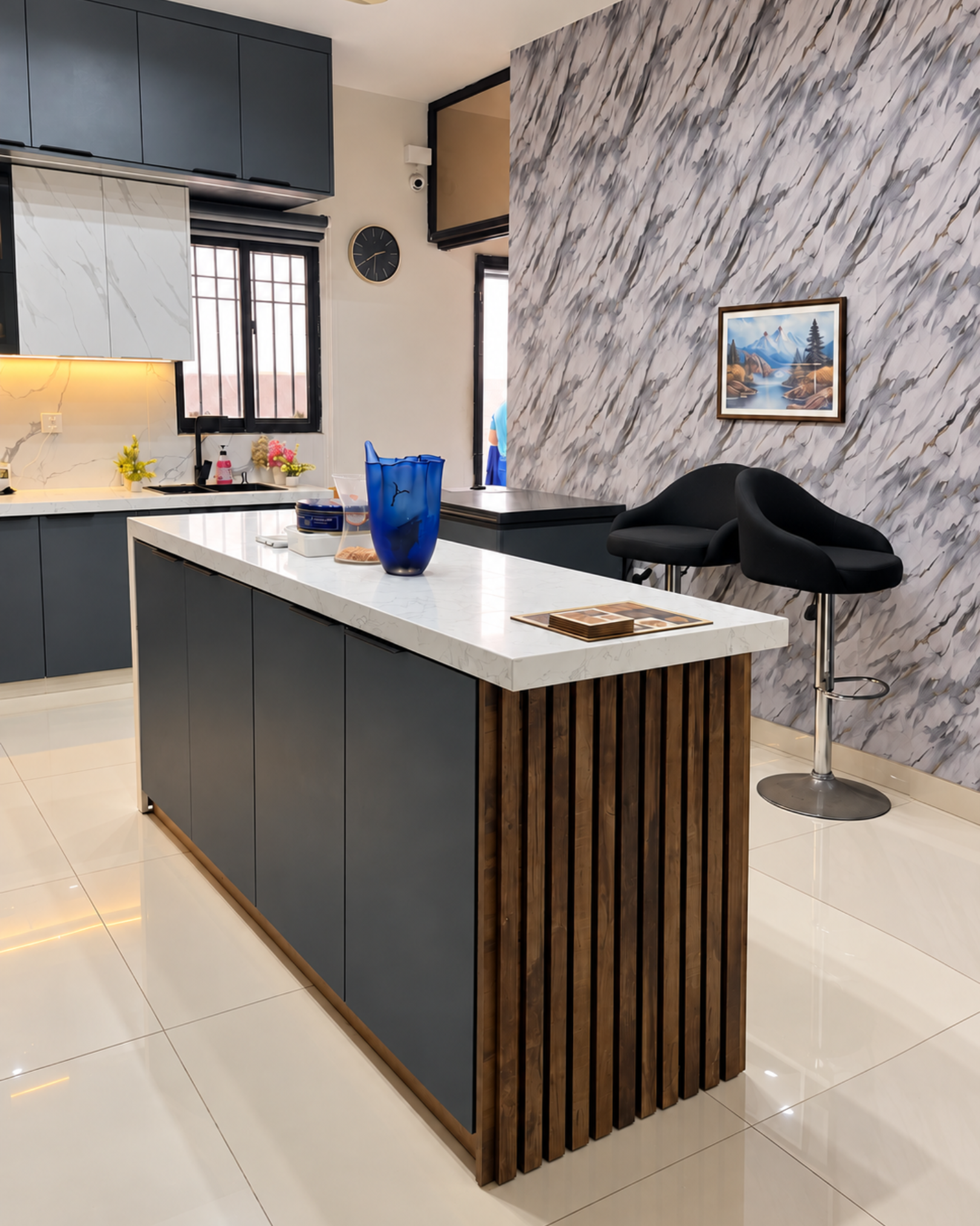 Kitchen island with charcoal storage cabinets, a wood slat end and white countertop beside two black bar stools.