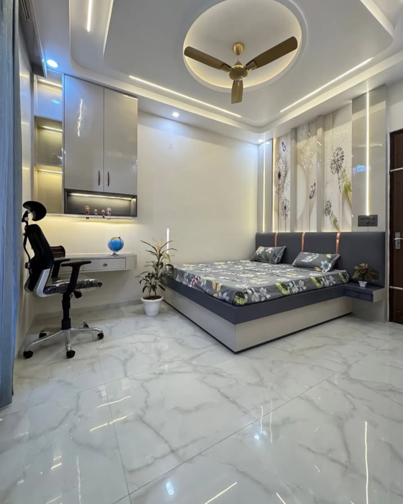 Bedroom with a grey upholstered bed, floral feature wall, floating study desk and illuminated overhead storage