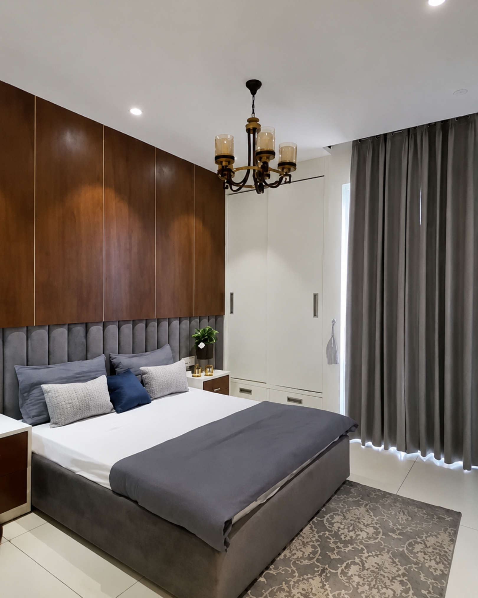 5 Grey upholstered bed beneath a wood-look feature wall, with a white sliding wardrobe, grey curtains and a chandelier.