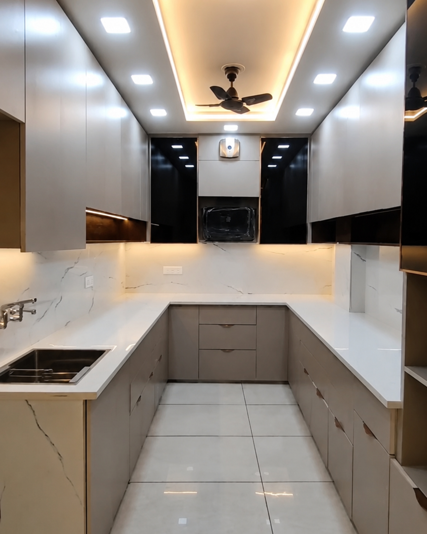 U-shaped kitchen with grey cabinets, glossy black doors, white countertops and an illuminated marble effect backsplash.