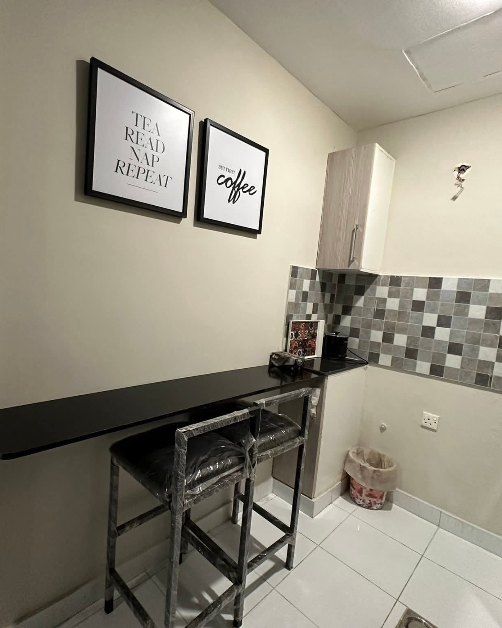 6 Compact coffee corner with a black breakfast counter, two bar stools, grey checkerboard backsplash and framed coffee prints.