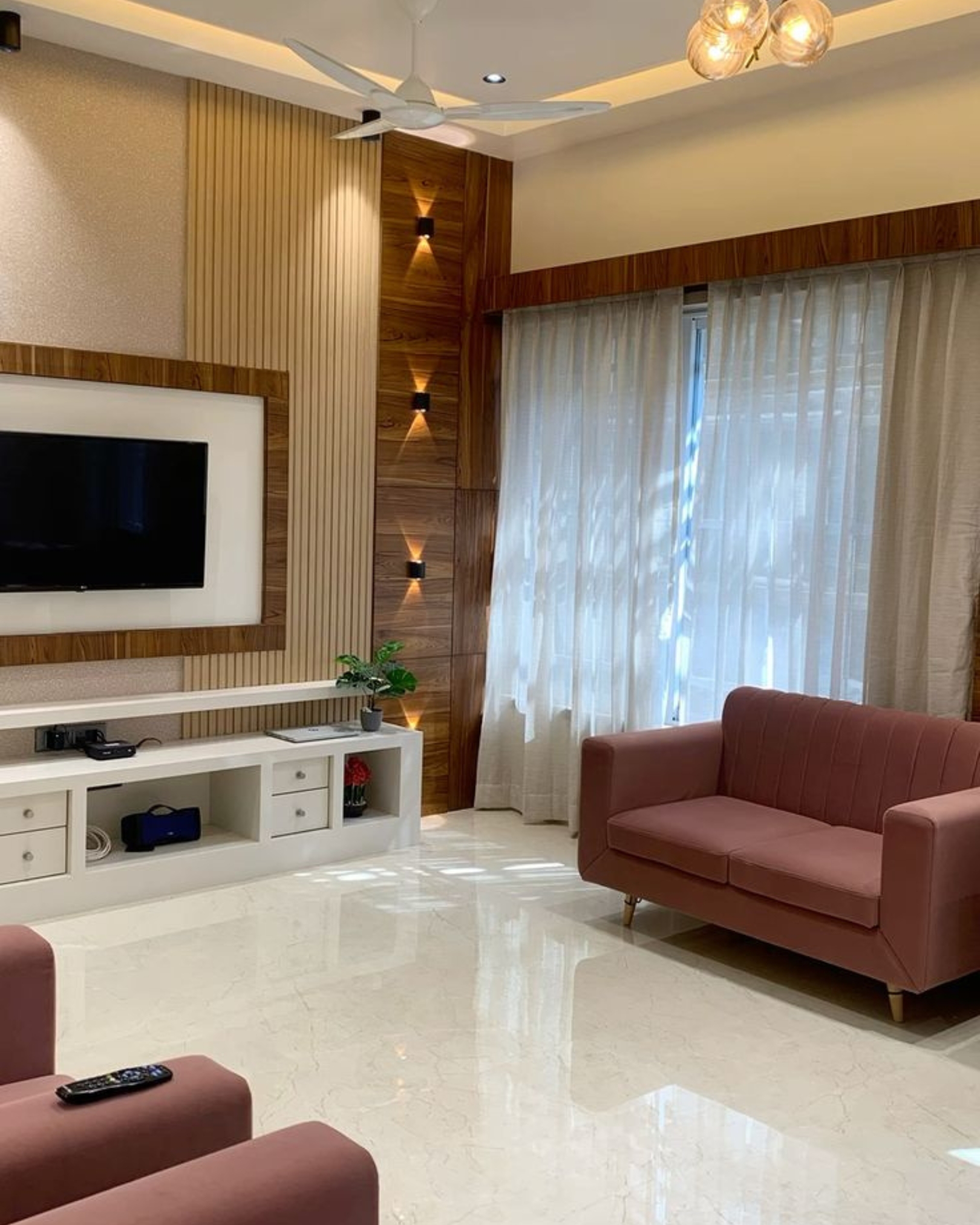 6 Soft pink sofa beside sheer curtains, a wood-look TV wall, cream fluted panels and warm wall lights.