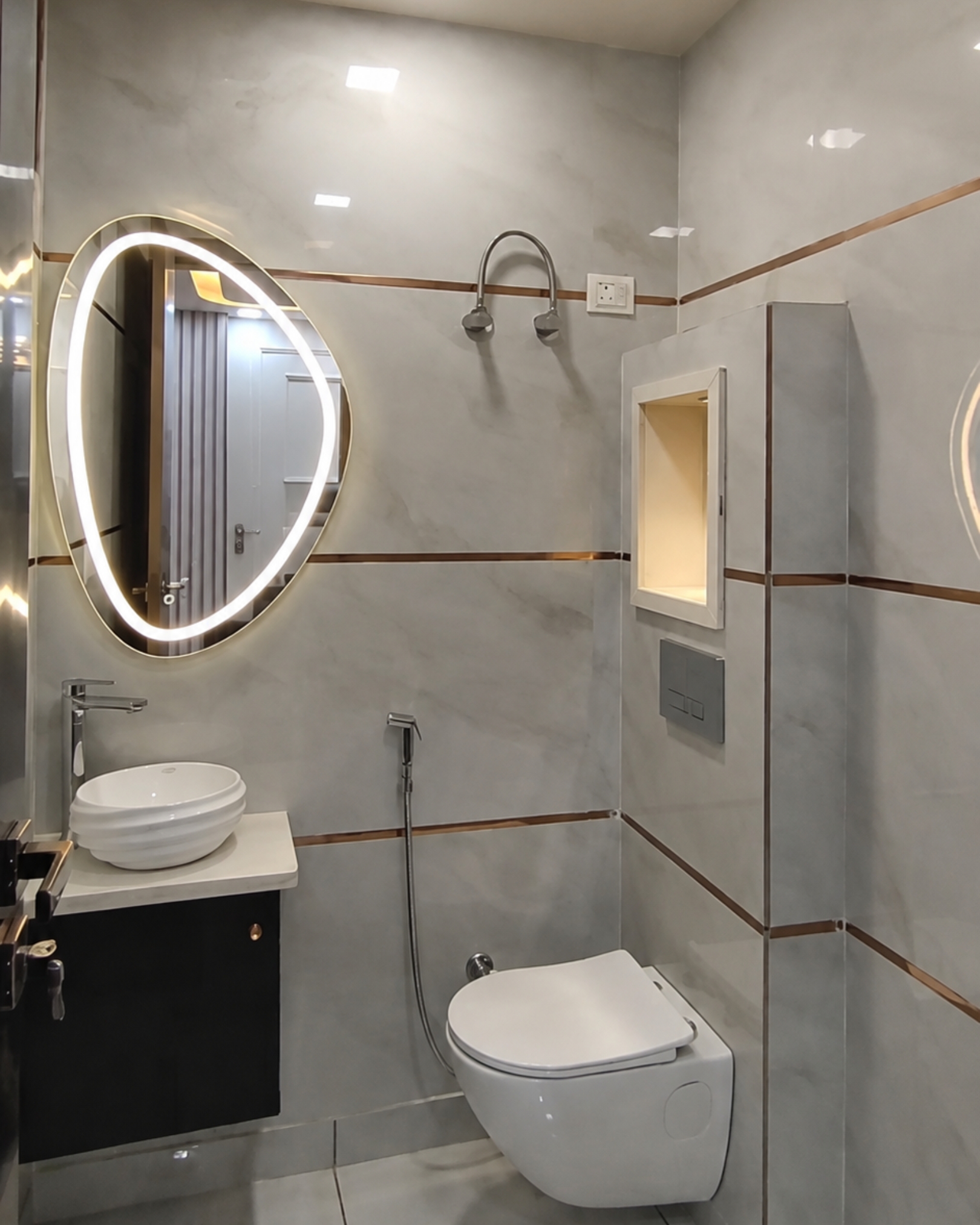 Bathroom with a curved illuminated mirror, ribbed white vessel basin, black vanity and a lit niche above the toilet.