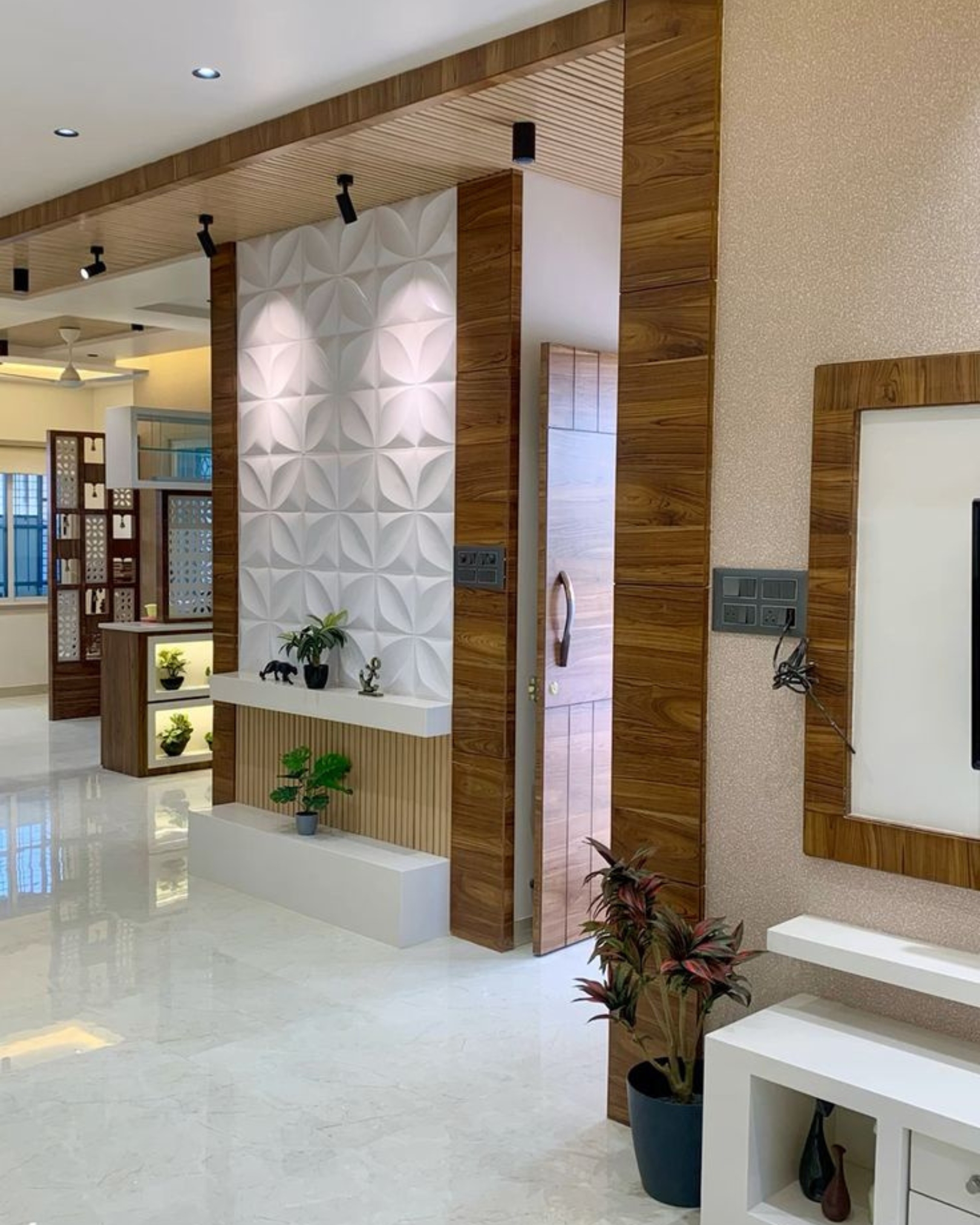 7 White geometric relief wall panels framed by wood-look finishes, with display ledges, plants and overhead spotlights.
