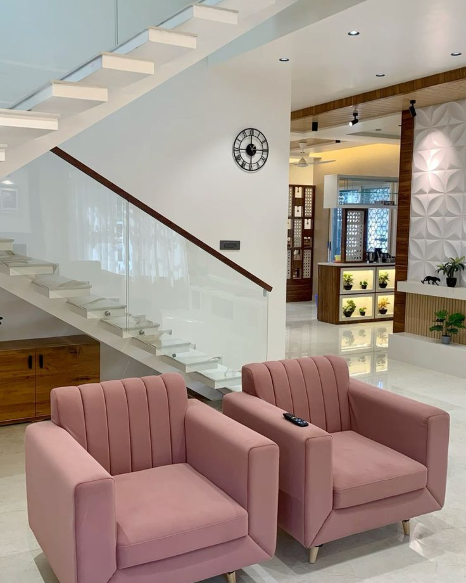8 Two pink upholstered armchairs beside a white staircase with a glass balustrade, wooden handrail and under-stair cabinet.