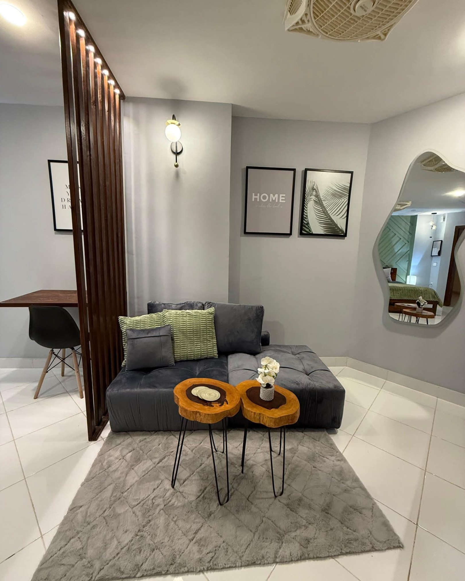 Compact sitting area with a grey chaise sofa, wooden slat partition, live-edge tables and an irregular wall mirror.
