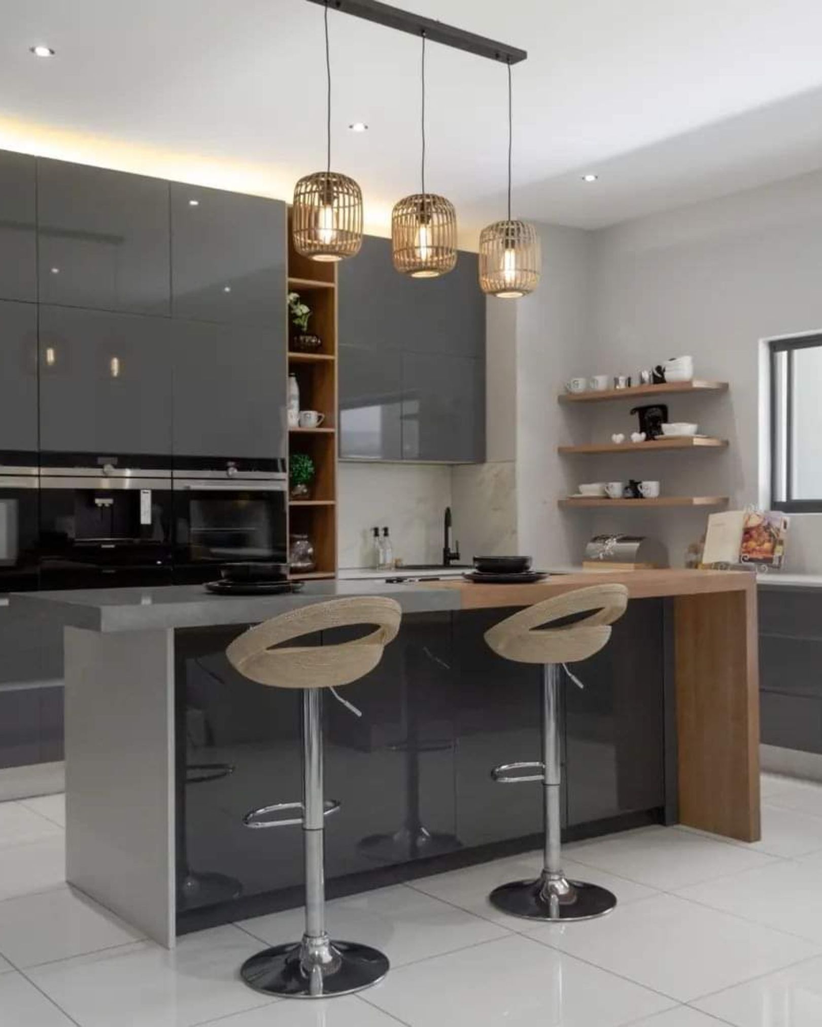 Modern kitchen with glossy charcoal grey cabinets, oak shelving, built-in appliances and a breakfast island with two stools beneath woven pendant lights.