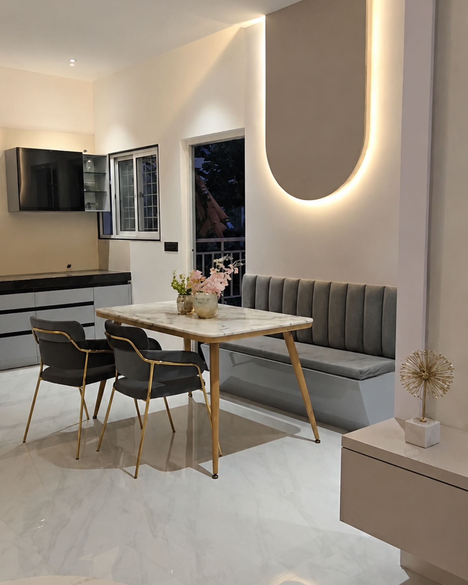 Dining nook with a grey upholstered bench, gold framed chairs and a marble effect table beneath a backlit wall feature.