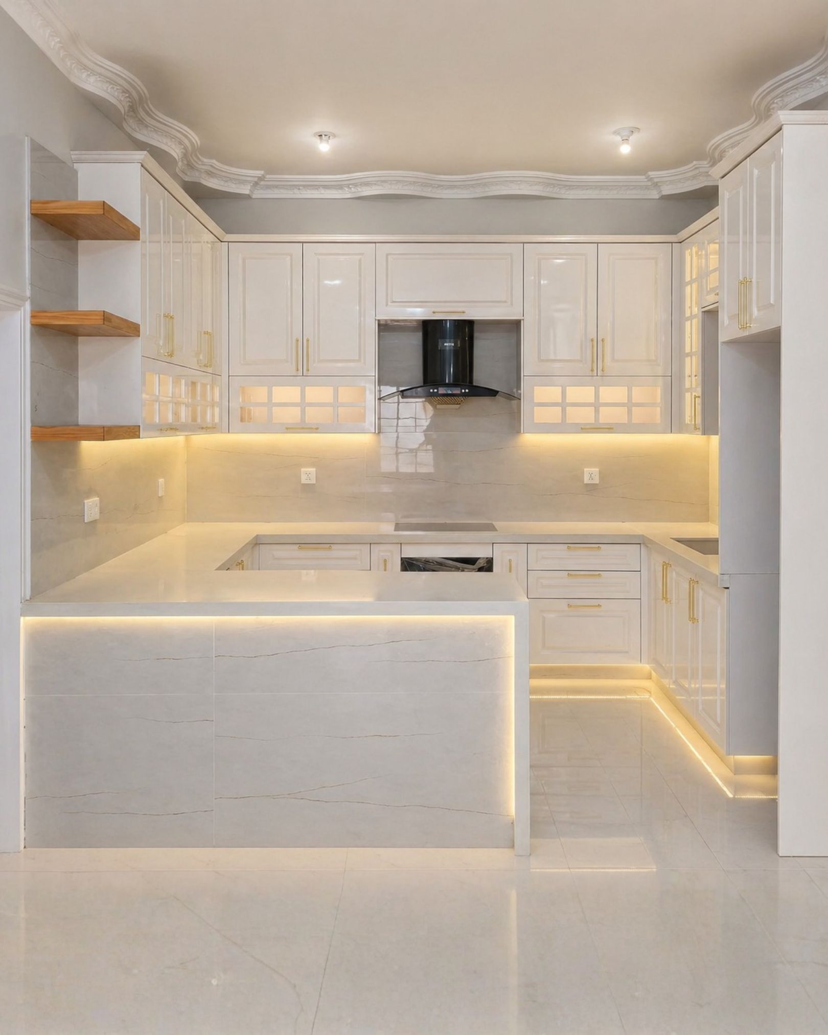 White raised panel kitchen cabinets with gold handles, illuminated glass doors, warm under cabinet lighting, wooden shelves and a marble effect peninsula.