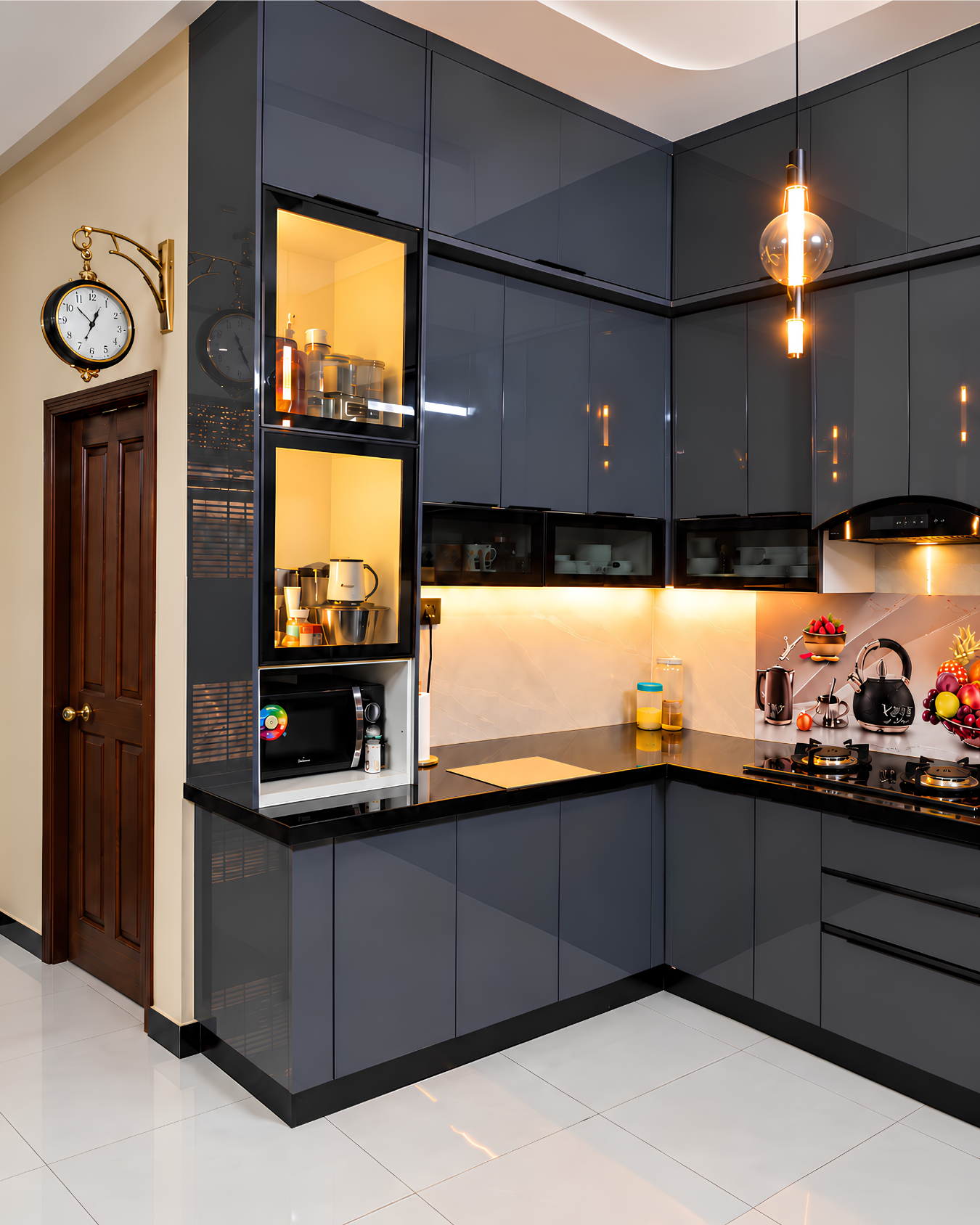 Corner view of glossy graphite cabinets with a tall illuminated glass display, microwave shelf and warm under cabinet lighting.