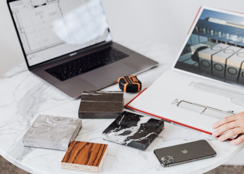 Designer reviews plans with laptop and material samples Designer reviews plans with laptop and material samples
